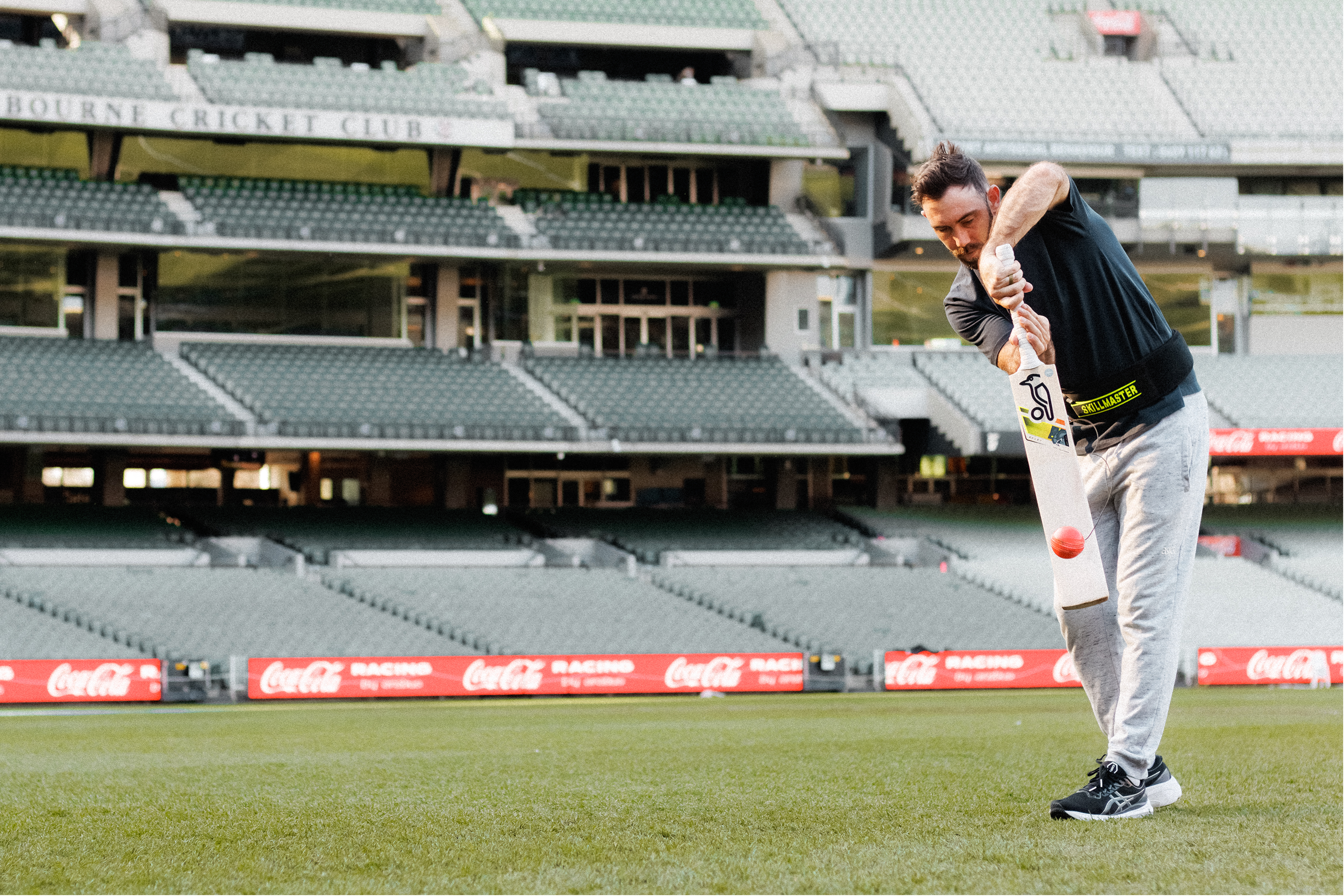 Middle aged male playing cricket on a sports field with stadium seats in the background